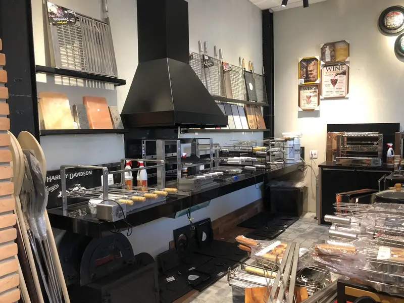 Showroom com coifa preta, churrasqueiras de inox montadas e utensílios em prateleiras