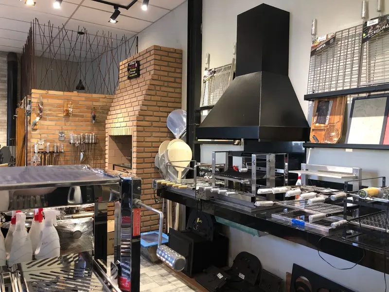Showroom com churrasqueira de inox e coifa preta montada, ao lado de parede de tijolinho