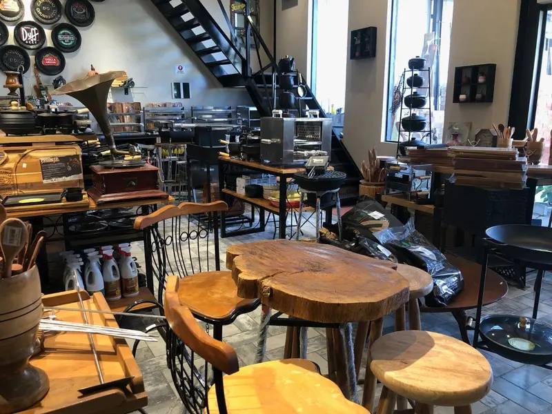 Showroom com mesa de madeira maciça, banquetas e churrasqueiras ao fundo