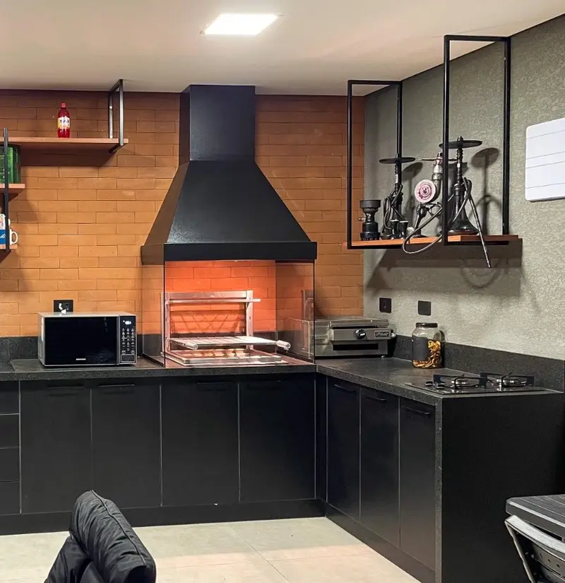 Cozinha gourmet com coifa preta, parede de tijolinho e churrasqueira ao centro