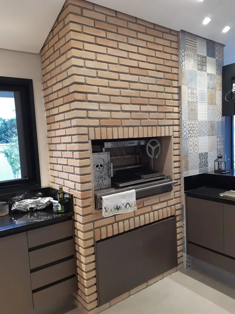 Churrasqueira de tijolinho aparente com grill giratório, ao lado de bancada