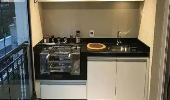 Churrasqueira compacta de inox em bancada preta com cuba, atrás de vidro