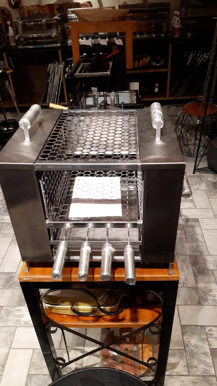 Grill de inox com espetos giratórios em carrinho de ferro preto